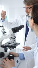 Two scientists, a man and a woman, in lab coats and protective gear, conduct research in a sterile...
