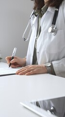 Professional female doctor wearing white lab coat and stethoscope documenting patient information...