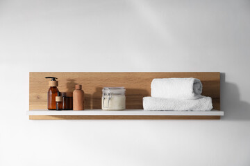 Wooden shelf with cosmetic products and towels on white background