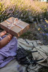 Girl in lavender dress holding a gift box with ribbon, sitting among blooming lavender flowers....