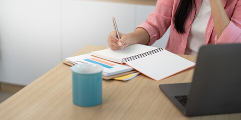 Work from home Woman writing notes while on a phone call in a bright workspace.