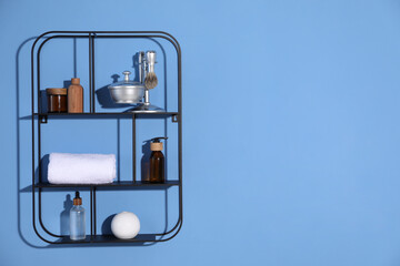 Metal shelving unit with towel and cosmetic products on blue background. Space for text