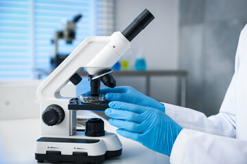 Scientist researching soil sample with microscope at white table in laboratory, closeup