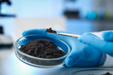 Scientist taking soil sample for research at white table in laboratory, closeup