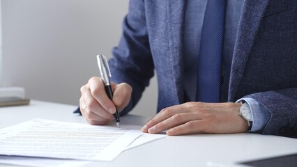Professional businessman signing contract with silver pen, wearing tailored blue suit, business...