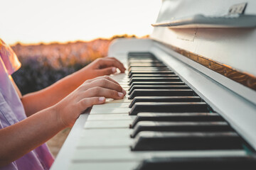 Child playing piano in lavender field at sunset. Close-up of hands on keyboard, white piano and...