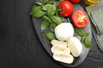 Tasty mozzarella cheese, tomatoes, basil and spices on black table, flat lay. Space for text