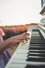 Child playing piano in lavender field at sunset. Close-up of hands on keyboard, white piano and...