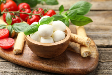 Tasty mozzarella cheese balls, tomatoes, basil and grissini on wooden table, closeup
