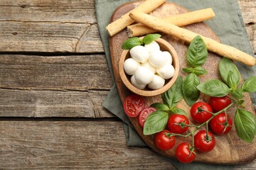 Tasty mozzarella cheese balls, tomatoes, basil and grissini on wooden table, top view. Space for text