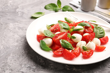 Tasty salad Caprese with mozzarella, tomatoes, basil and spices on grey table, closeup. Space for...