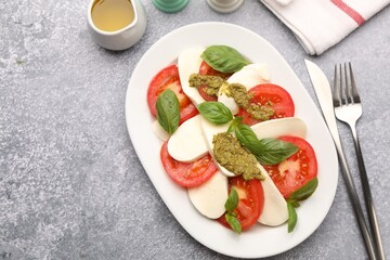 Tasty salad Caprese served with pesto sauce on grey table, flat lay. Space for text