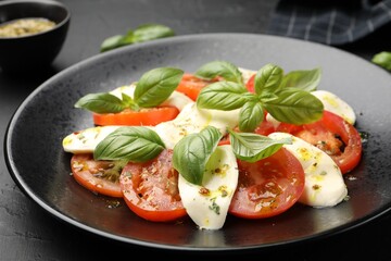 Tasty salad Caprese with mozzarella, tomatoes, basil and spices on black table, closeup