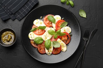 Tasty salad Caprese with mozzarella, tomatoes, basil and spices on black table, flat lay