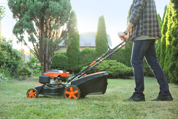 Man cutting green grass with lawn mower in garden, closeup