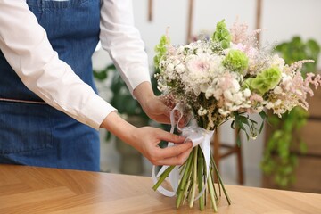 Florist making bouquet of flowers at wooden table indoors, closeup