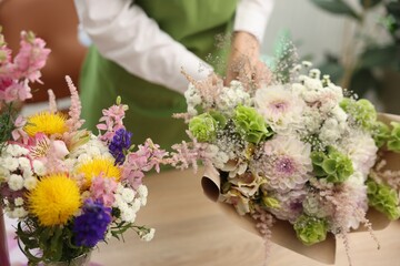 Florist making bouquet of flowers at table indoors, closeup