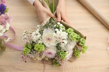 Florist making bouquet of flowers at wooden table, above view