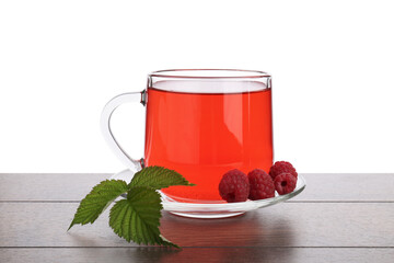 Aromatic raspberry tea in glass cup, berries and green leaves on wooden table against white...