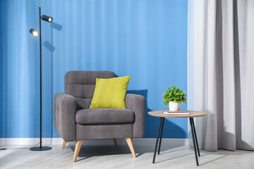 Comfortable armchair, lamp and houseplant near blue wall indoors
