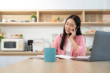 Work from home Smiling woman on phone while writing in her home office.