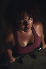 Sweaty plus-size woman lifting weights in gym, viewed from above, confident and determined, dark indoor background, suitable for fitness promotions and motivational content. challenge, fierce, topview