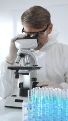 Male virologist in medical gown and gloves examines virus samples under microscope while conducting...