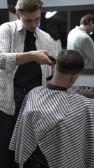 Professional barber carefully trimming customer's hair with electric clipper, providing a stylish...