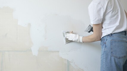 Unknown female construction worker applying plaster with putty knife, smoothing wall surface during home renovation, fixing wall imperfections with professional drywall repair technique, close up