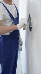 Professional construction worker wearing blue work overall is using a finishing trowel to carefully apply plaster on a wall, demonstrating expertise in home renovation