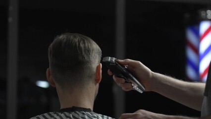 Skilled barber trimming client's hair with electric razor, creating precise contemporary hairstyle...