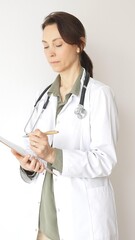 Doctor woman wearing stethoscope and white coat over green blouse is standing and writing on a...