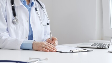 Doctor woman completing healthcare paperwork, clipboard positioned near laptop and stethoscope in...