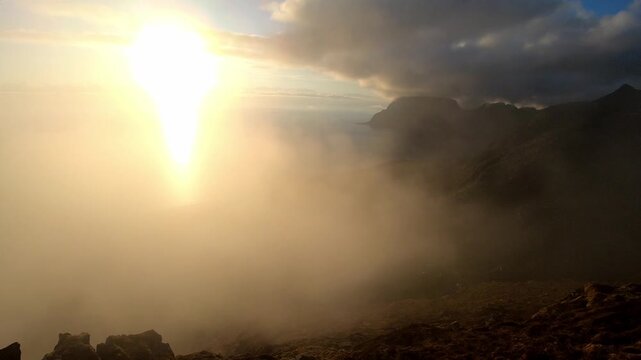 Fog rolls over mountains above Utakleiv during midnight sun timelapse from Mannen in Lofoten
