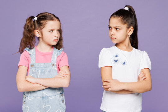 Little angry mad offended two friends kids children girls 9-10 year old wear casual clothes together hold hands crossed folded look to each other isolated on plain purple background Lifestyle concept