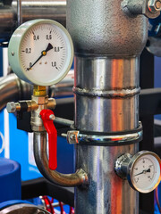 Detailed view of industrial pressure gauge and valve in a manufacturing facility during daylight...