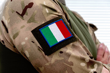 A man in an army uniform with an Italian flag on his sleeve and army badges.