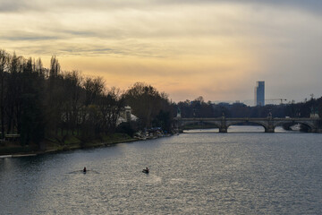 Elevated view of the Po River at sunset, with a pair of rowers, Umberto I Bridge and Piedmont Region Headquarters skyscraper in the background, in winter, Turin, Piedmont, Italy