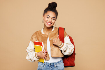 Young smiling happy teen girl student wear casual clothes backpack bag hold books showing thumb up like gesture isolated on plain pastel light beige background. High school university college concept.