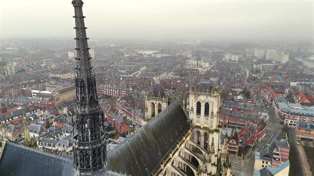 Drone view of the central spire and Gothic architecture of Amiens Cathedral with surrounding old town buildings under a cloudy sky in Hauts de France 