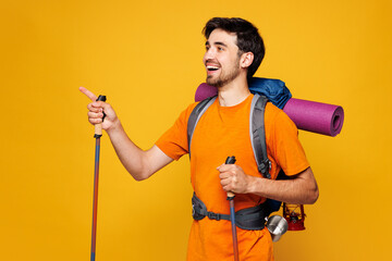 Young fun traveler man carry backpack with stuff mat trekking poles isolated on plain yellow...