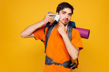 Young traveler man carry backpack with stuff mat shaving with ax isolated on plain yellow...