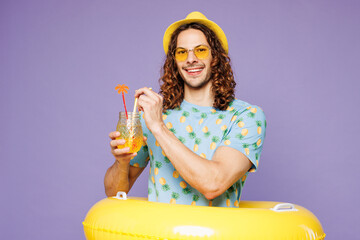 Young fun man wear blue beach t-shirt yellow hat sunglasses rest near hotel pool hold rubber ring...