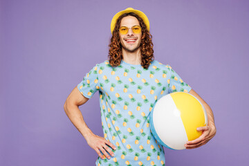 Young happy smiling man wear blue beach t-shirt yellow hat sunglasses rest near hotel pool hold in...
