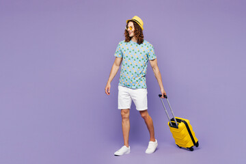 Traveler young man wear blue clothes hold suitcase bag walk isolated on plain purple background....