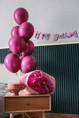Birthday celebration setup in a bedroom with pink balloons, fresh peonies bouquet, and a pink cake...