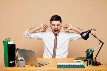 Young employee business man wear white shirt tie sit work at office desk with pc laptop cover ears...