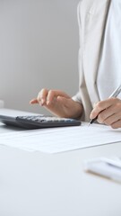Businesswoman is calculating annual tax using calculator and taking notes in the office, managing...