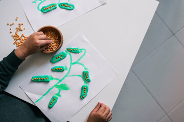 Top view of a child crafting a green plant using modeling clay and lentils. The hand reaches for a...