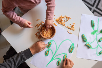 Children’s hands playing with dry lentils and modeling clay, creating a plant-themed craft on...